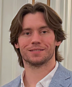 nick headshot with long blond hair beard blue suit