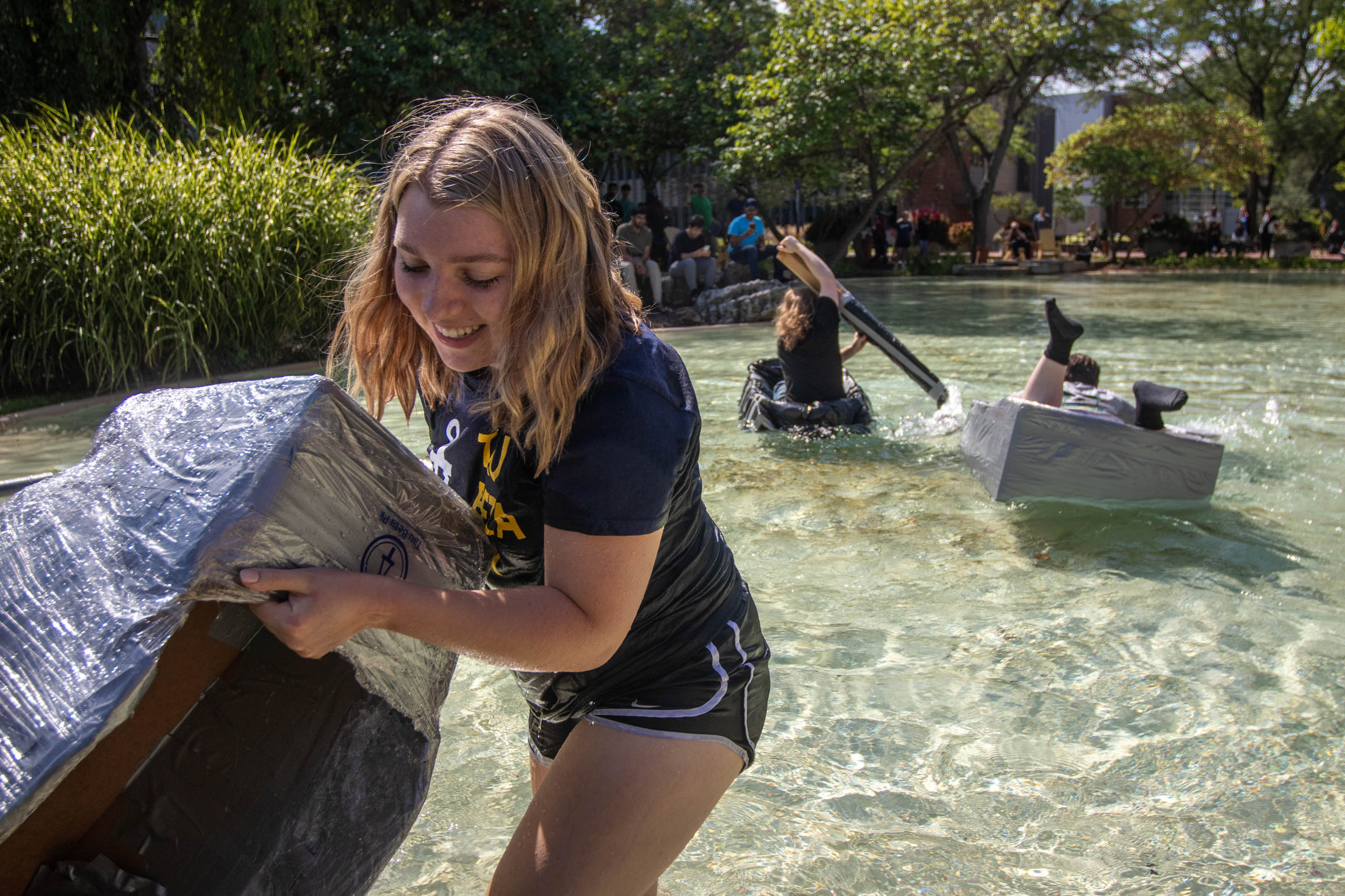 A student pulls her cardboard boat of Chancellor's Pond, while other students in cardboard boats struggle in the background 