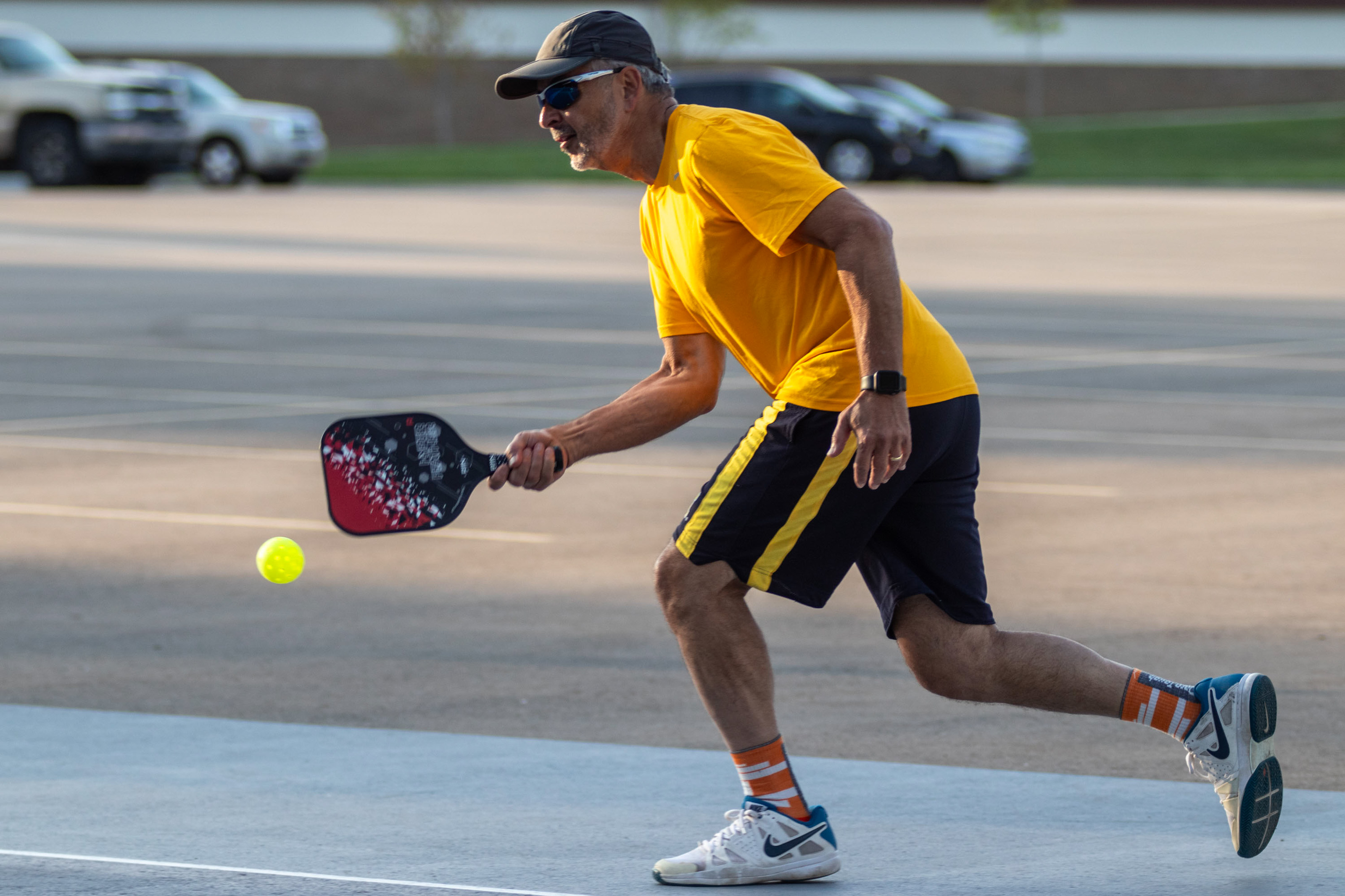 Chancellor Grasso bends down for a forward shot on the pickleball court