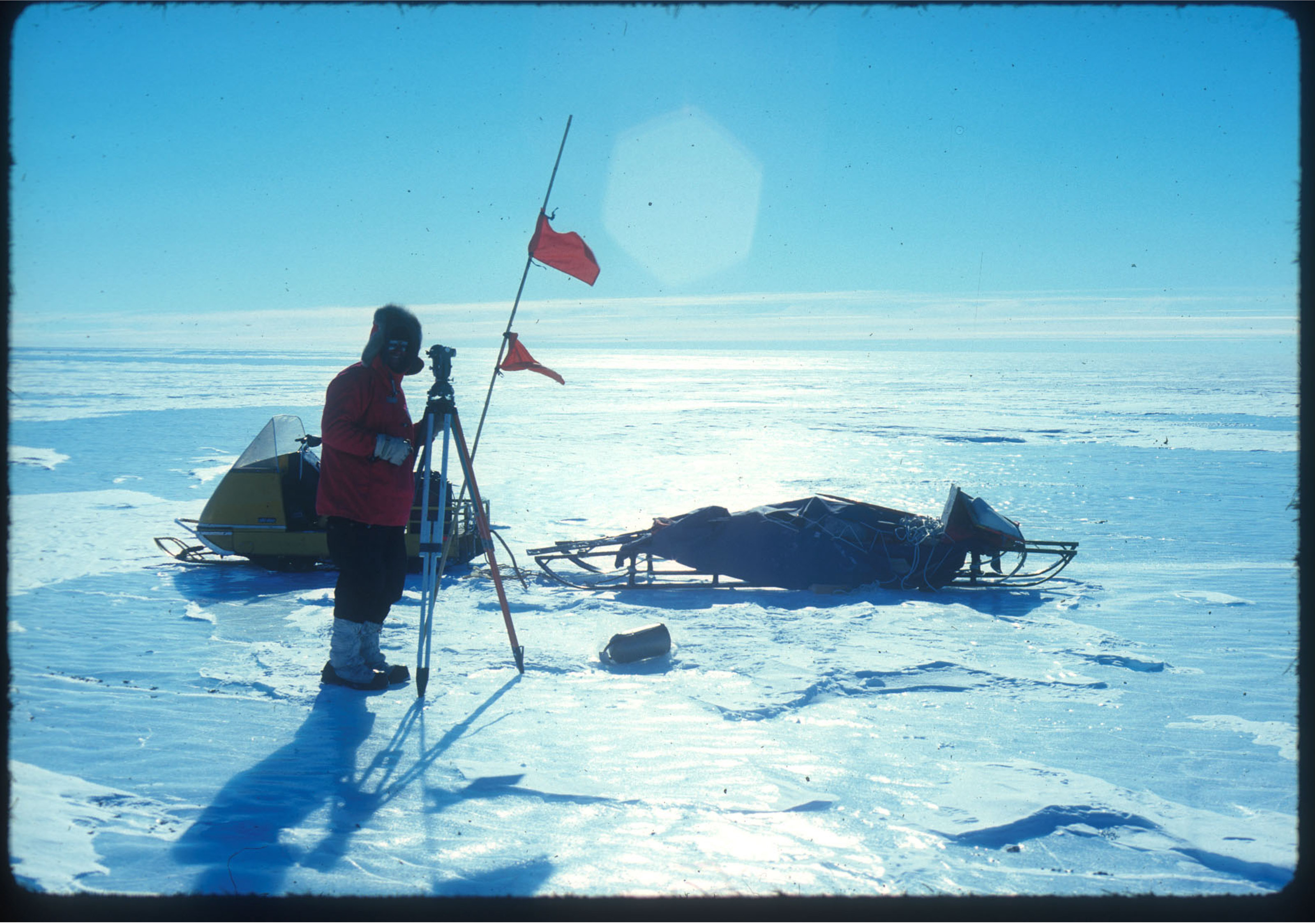 England in Antarctica, standing next to survey equipment, a snowmobile and sled.