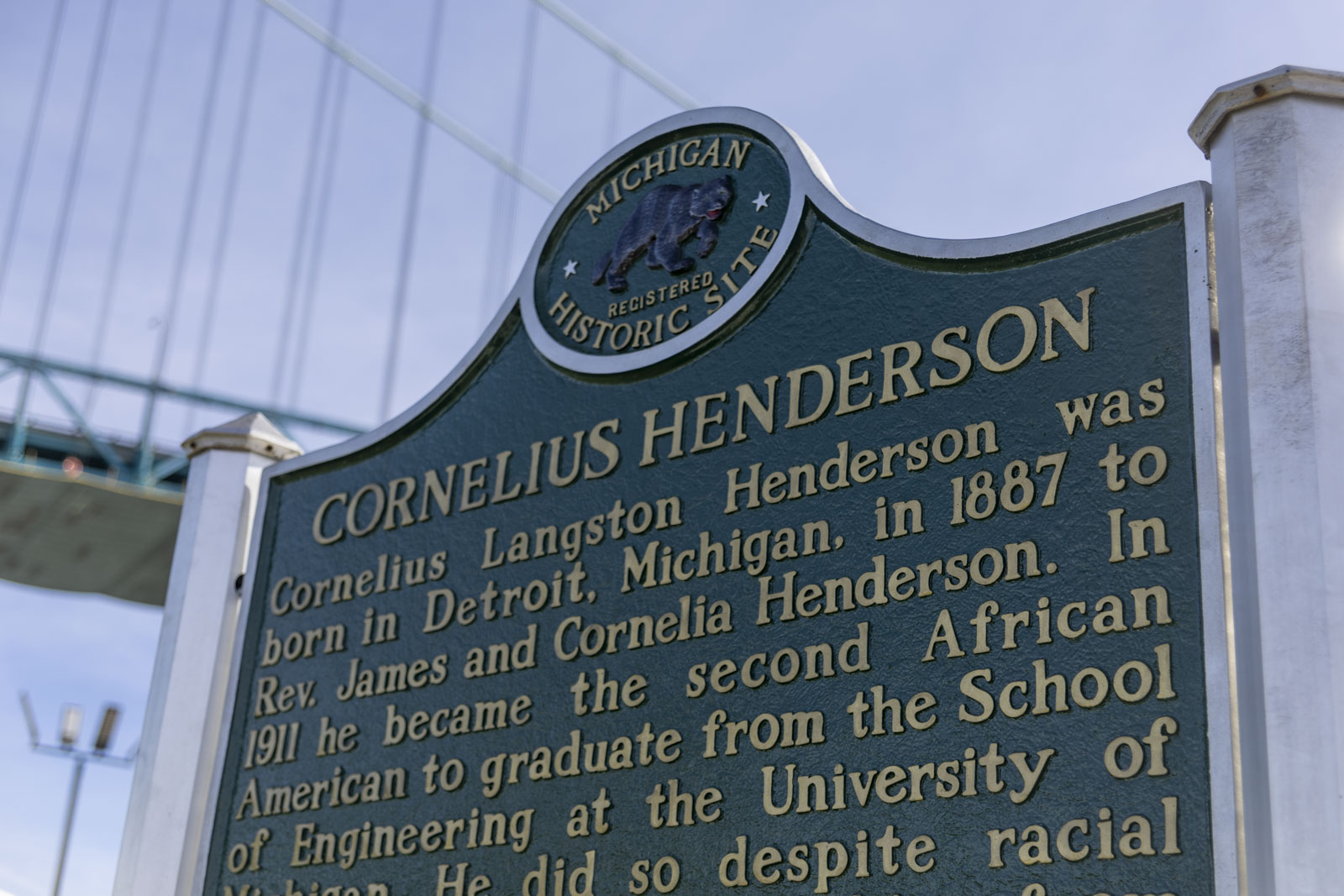 A historical marker honoring Cornelius Henderson with the Ambassador Bridge in the background