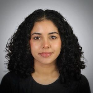 Head-and-shoulders portrait of a person with shoulder-length curly dark hair, wearing a black top.