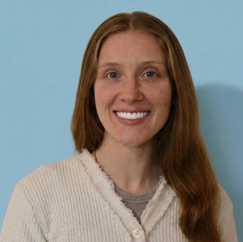 An individual in a white shirt sitting with a smile.