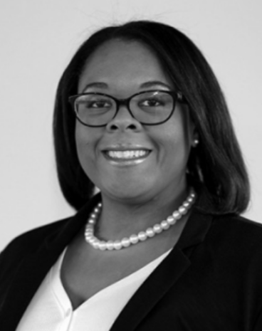 A black-and-white professional headshot of a woman wearing glasses, a pearl necklace, and a blazer over a light-colored top. She is smiling and facing the camera.