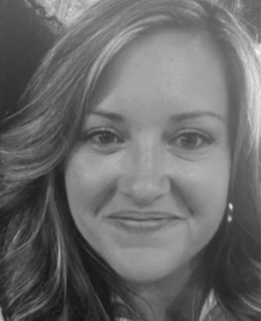 A black-and-white close-up portrait of a woman with wavy shoulder-length hair, smiling gently at the camera.