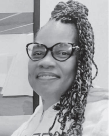A black-and-white portrait of a woman smiling at the camera, wearing glasses and a hoodie. Her hair is styled in long braids pulled into a top bun.