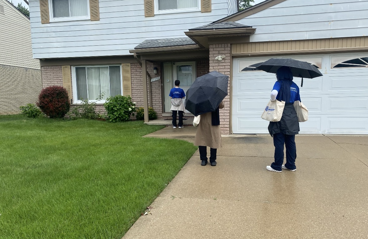 Student interns participating in the Rep. Rashida Tlaib Democracy Summer Fellowship canvass a neighborhood in the rain, carrying umbrellas and campaign materials as they go door-to-door to engage with community members.