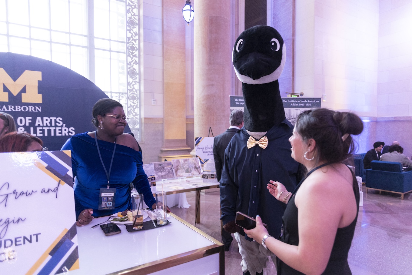 Two women speak to a student in a goose costume