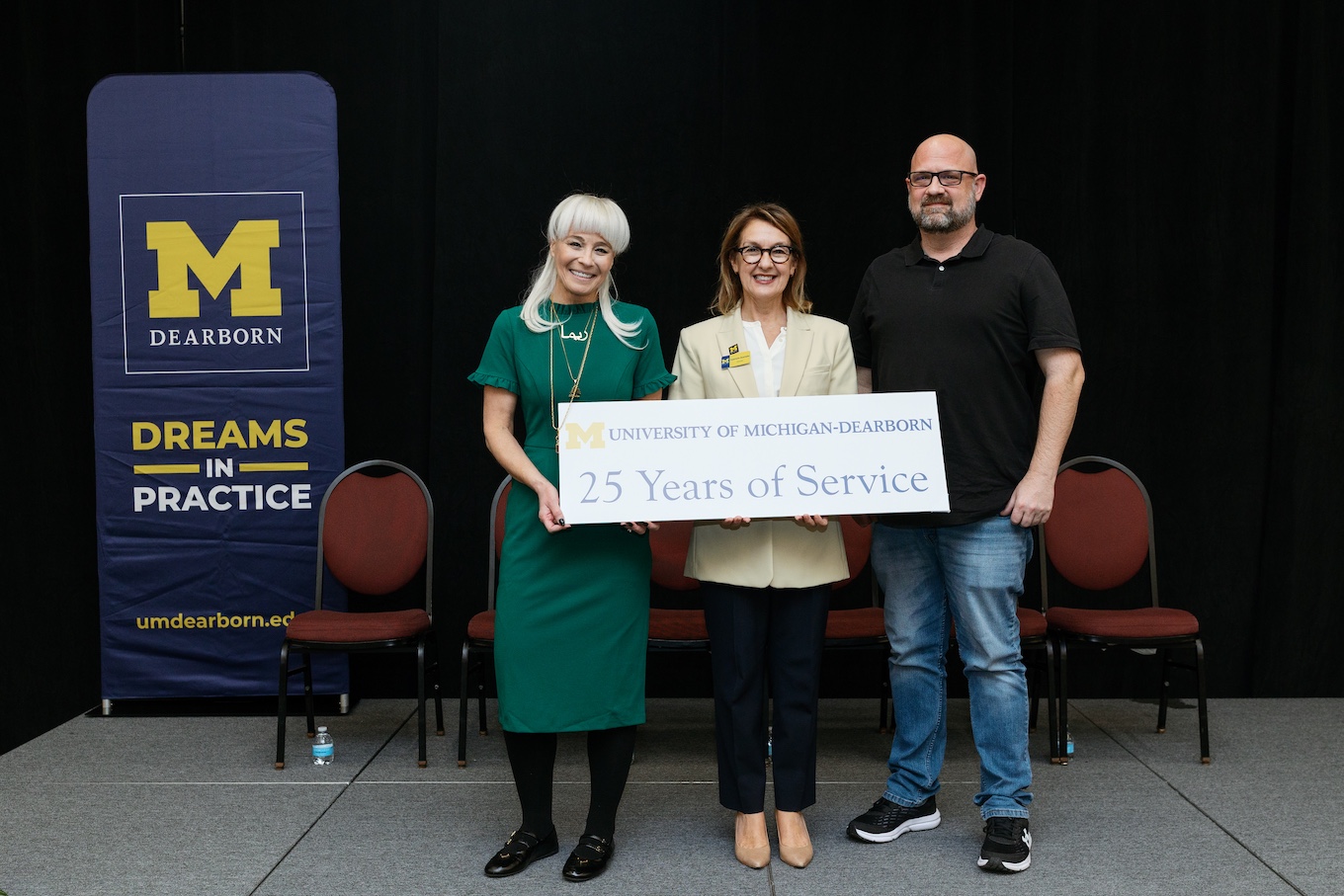 A group of well-dressed staff stand together with a sign that reads "25 Years of Service"