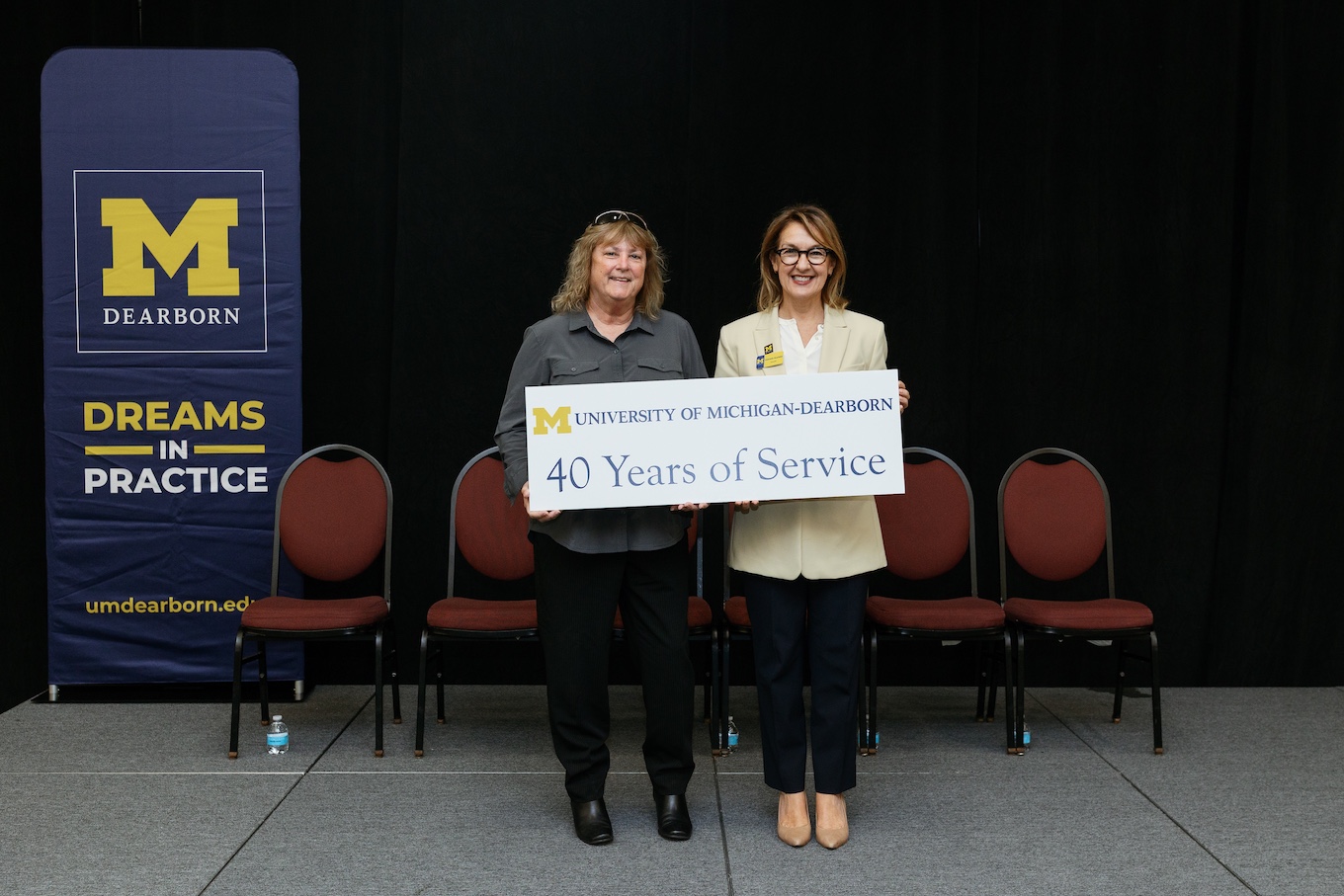 Two well-dressed staff members stand together with a sign that reads "40 Years of Service"