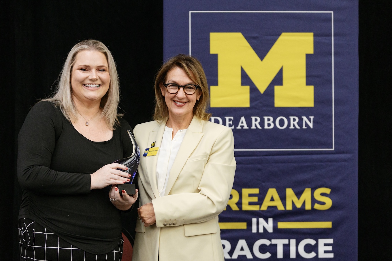 Two women take a photo together while holding a blue glass trophy for staff excellence