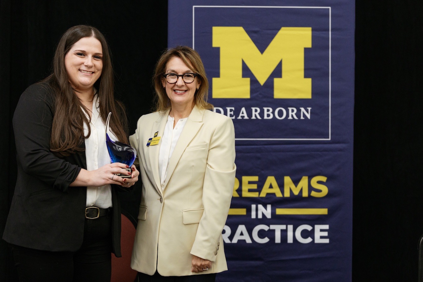 Two women stand next to each other holding a blue-tinted glass award