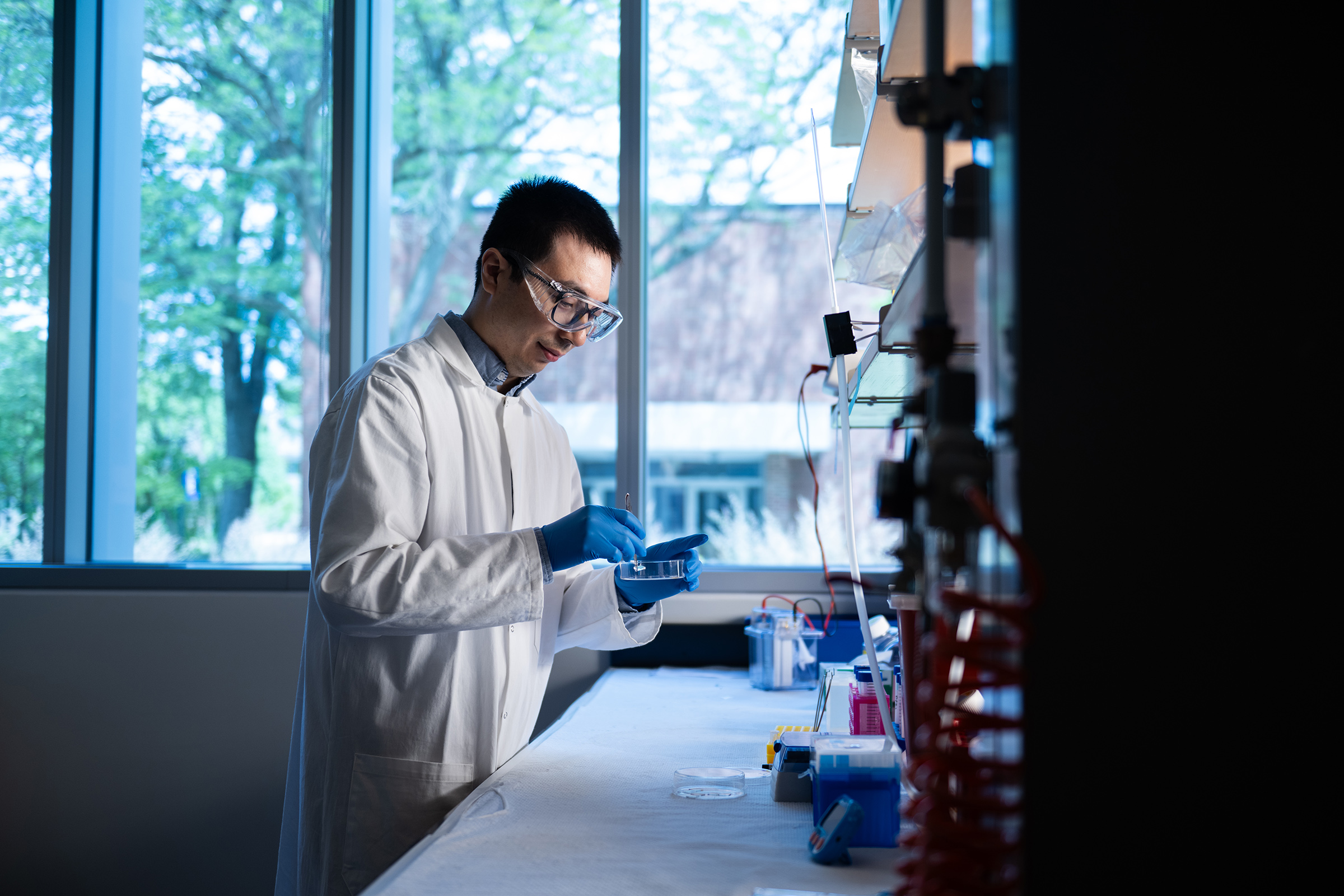 Wearing a white lab coat and protective equipment, Assistant Professor Jie Fan works in his cancer research lab