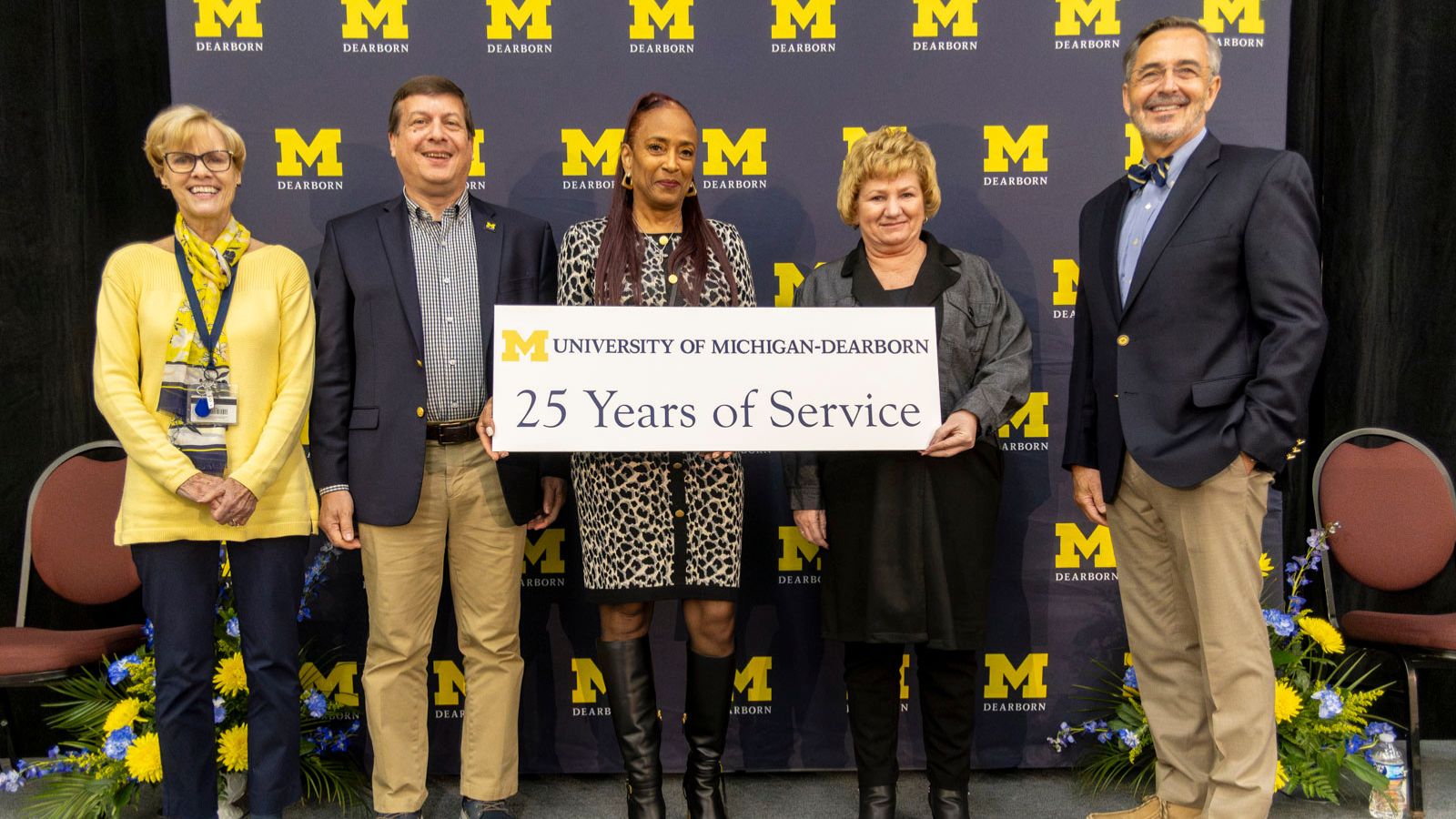 Staff receiving recognition for 25-years of service pictured on stage with Chancellor Grasso in front of a UM-Dearborn background