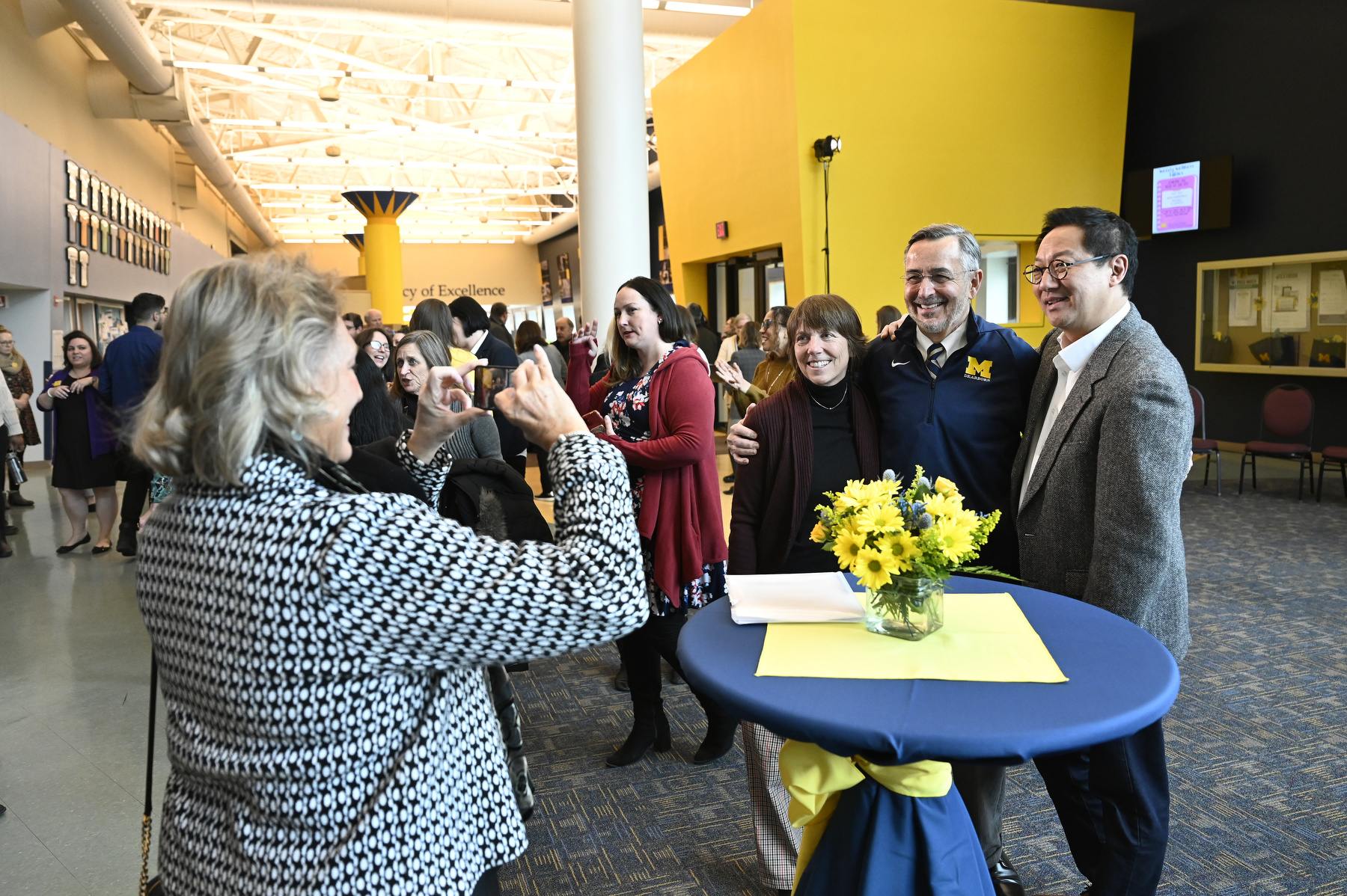 Susan Grasso, Chancellor Domenico Grasso and U-M President Santa Ono pose for a photo while hundreds of people mingle in the background at a reception in the University Center.