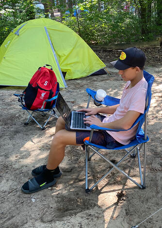 Student Anthony Pyrozhenko, son of Associate Professor of Public Administration Vadym Pyrozhenko, logs in for a virtual tutoring session from his campsite.