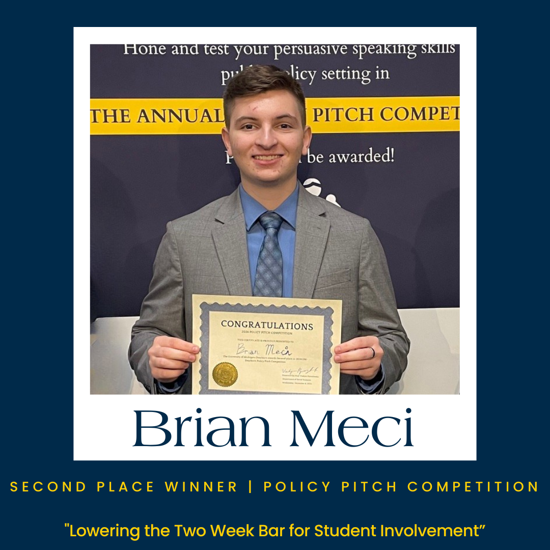 Policy Pitch Winner stands with award, smiling in grey blazer with text that says “second place winner, policy pitch competition”