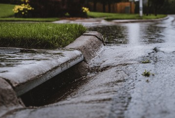 Rain going down a storm drain in the curb.