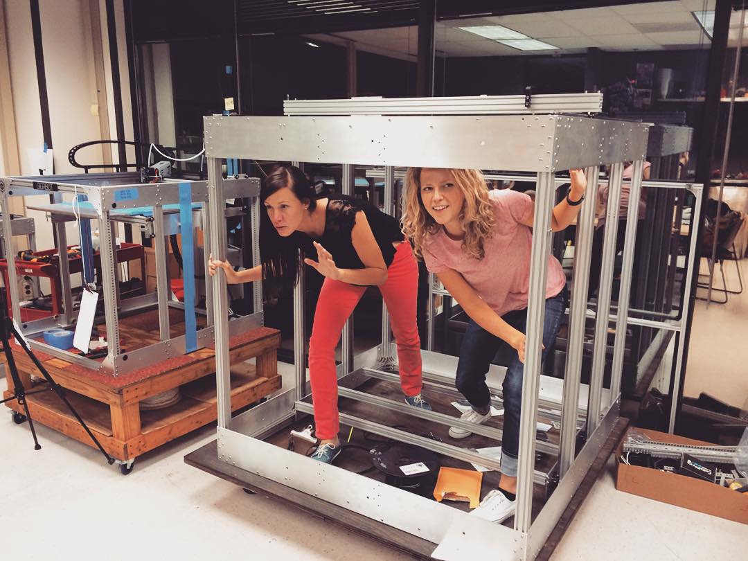 Snabes and a co-worker standing instead the metal frame of their large format 3D printer.