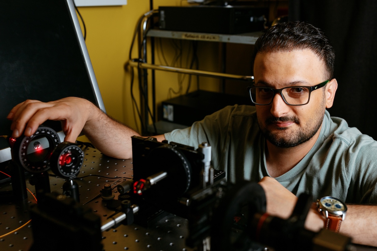 A researcher with glasses adjusts optical equipment with glowing red lasers on an optics table in a laboratory setting.