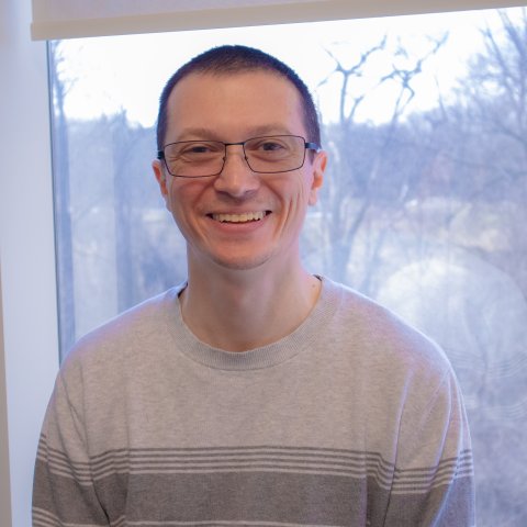headshot of smiling person with grey shirt and glases