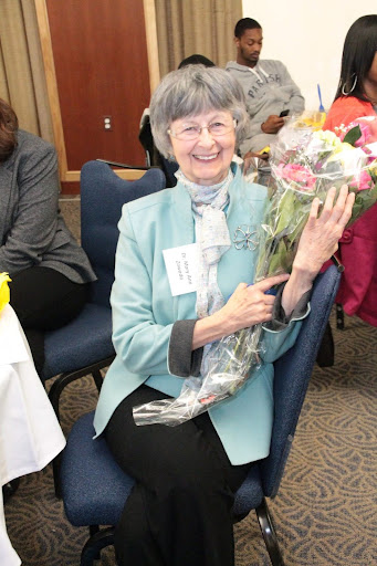 a photo of Mary Ann Zawada at an event in a banquet center holdiing a boquet of flowers smiling