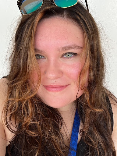 a smiling person with brown hair wears sunglasses on her head and a black tank top
