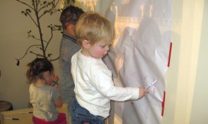 3 children drawing on paper attached to wall