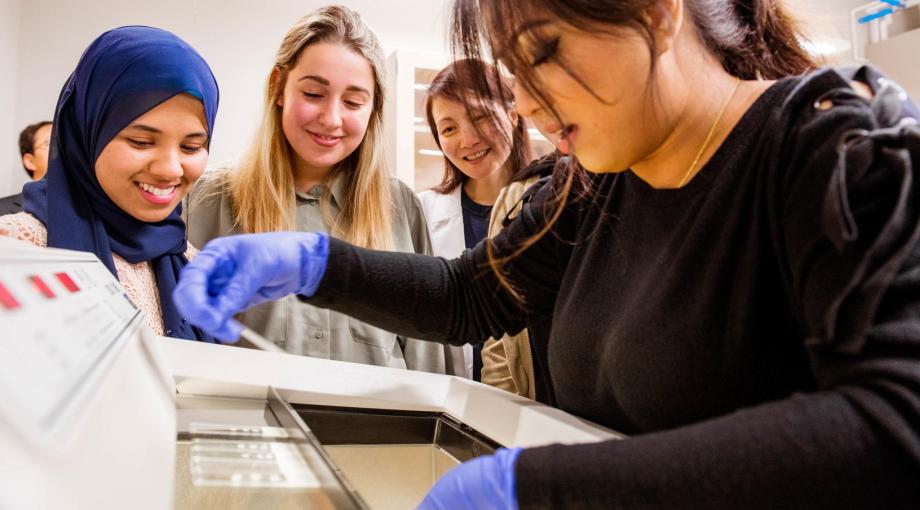 Through an Mcubed research project, Assistant Professor Zhi “Elena” Zhang (third from left), shows students (from left) Samiha Ishrat, Carissa Root and Kanika Karmaker how to use the lab’s cryostat machine, which thinly slices tissue so it can be examined under a microscope.