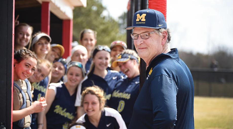 Kirk Philipich wearing Michigan baseball cap with female student-athletes standing behind him.
