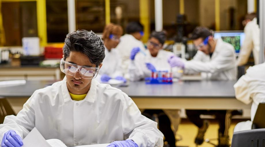 student wearing lab coat, goggles and gloves working in lab
