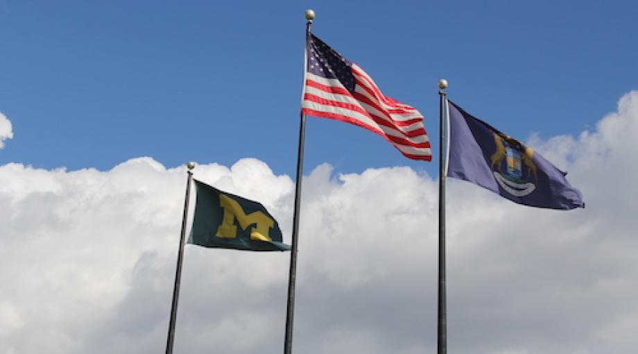 3 flags (US, State of Michigan and University of Michigan) fly in blue sky