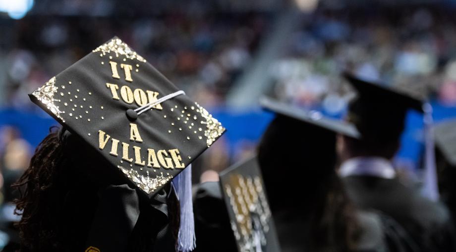 A student's graduation cap, bearing the slogan "I took a village," is photographed from behind during a commencement ceremony on the UM-Dearborn campus.