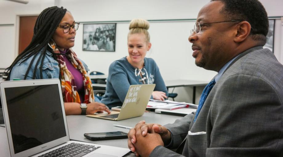 Two students and a Professor seating at a desk