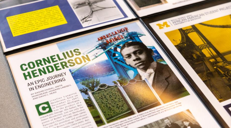 An angled shot of a poster board display featuring a historic photo of Cornelius Henderson, an image of the Ambassador Bridge and text about his life.