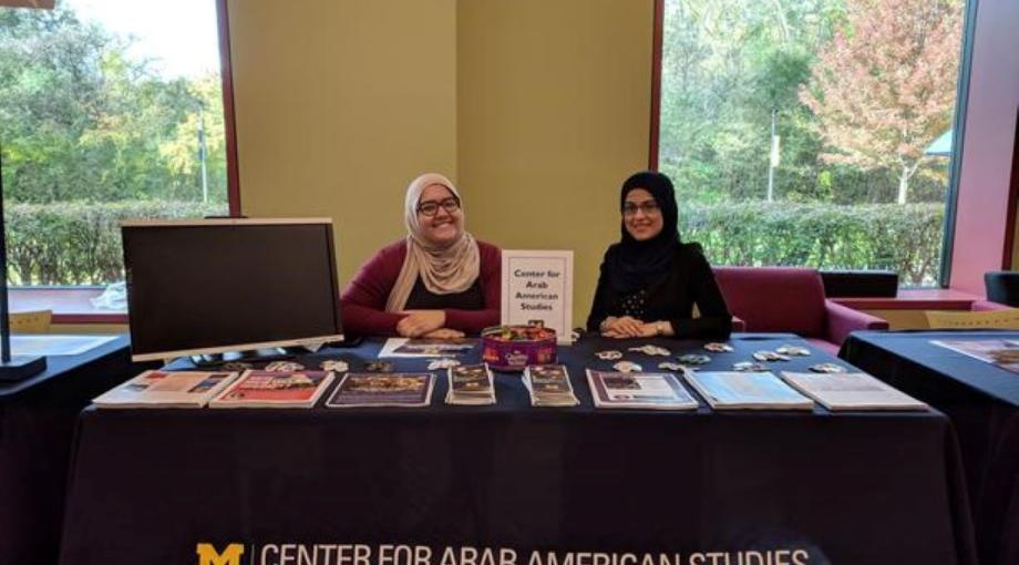 2 students sitting behind Center for Arab American Studies table.