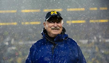 Tony England smiles, while standing in the snow at Michigan Stadium, wearing a UM-Dearborn ball cap.