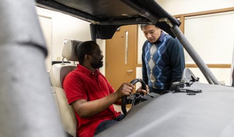 Associate Professor of Industrial and Manufacturing Systems Engineering Bochen Jia talks with a graduate student in a driving simulator.