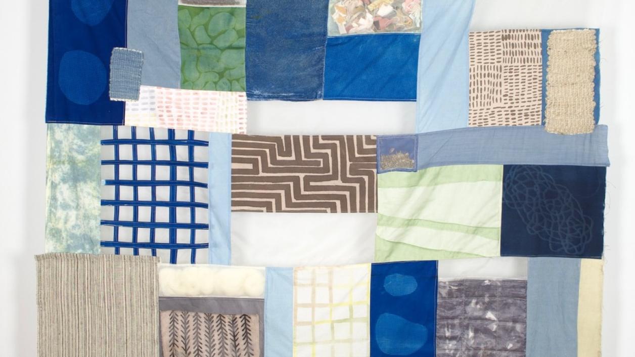 Hanging quilt with patches in blue, white, tan and green in a variety of patterns