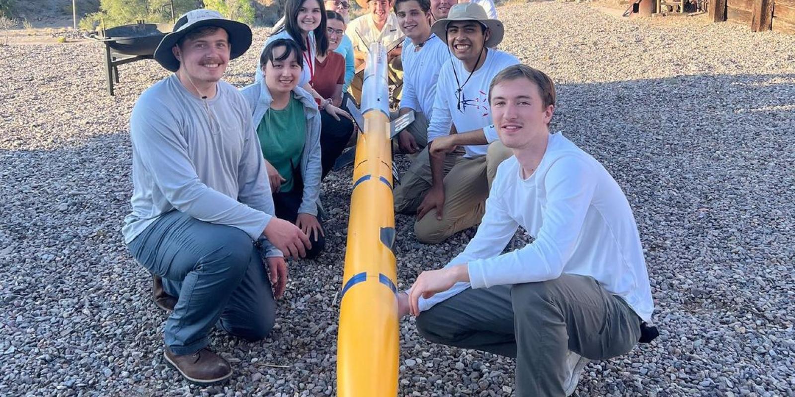 Members of the UM-Dearborn rocket team pose for a photo with their rocket in the New Mexico desert, with mountains in the background.