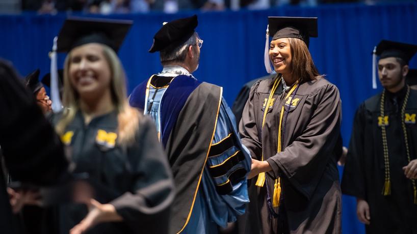 A women in graduation robes shaking hands with Chancellor Grasso