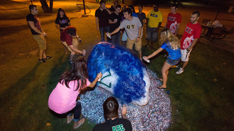Fraternity and sorority members painting the campus rock together.