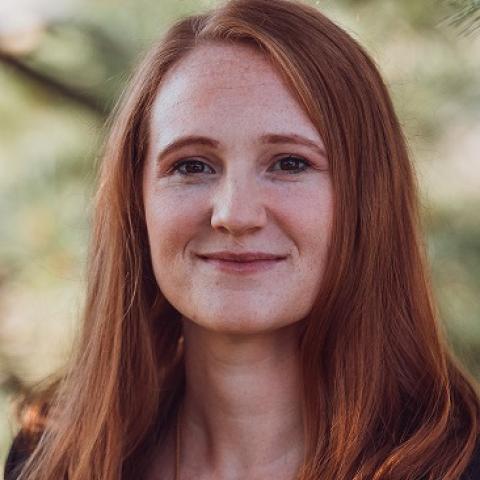 Laura Mallard Headshot with a conifer tree in the background.