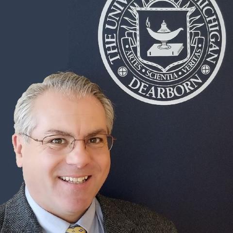 Tom Pitock standing below UM-Dearborn logo