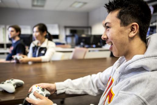 Up-close image of a student laughing while playing a video game with two more students in the background