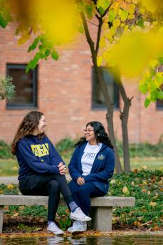 Two students sit together at a bench near Chancellor's pond