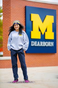 Female student wearing U-M clothing standing in front of M block