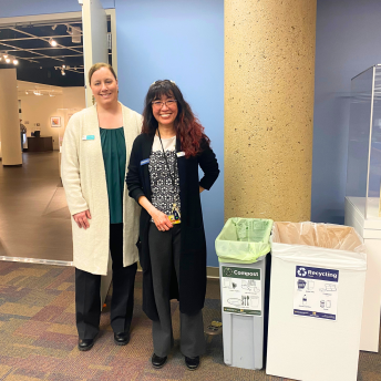 two staff members in front of a recycling and compost bin
