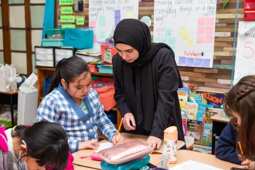 An individual helping a child with her worksheet.