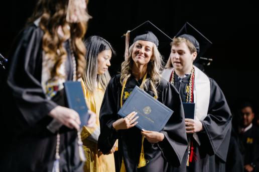 A proud, smiling female graduate accepting her dipolma during Commencement